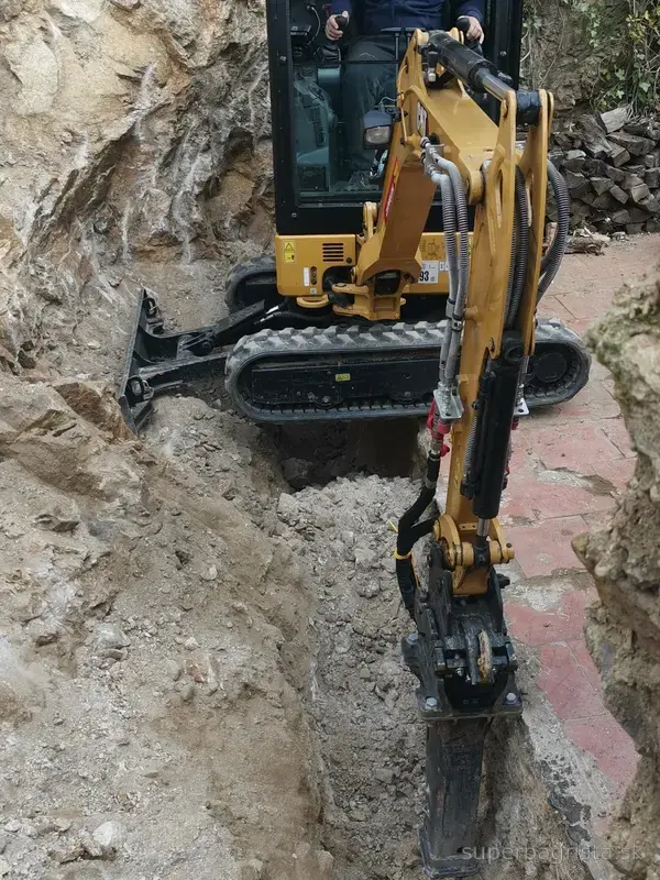 Minibáger CAT pri práci s kladivom v hlbšej skalnej ryhe
