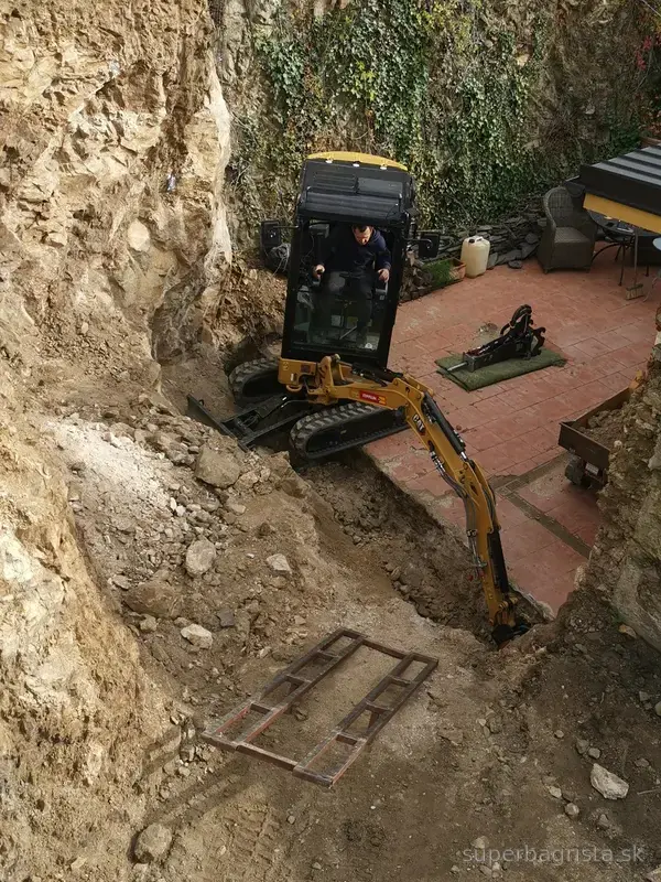 Pohľad zhora na minibáger CAT a výkop základu v skale