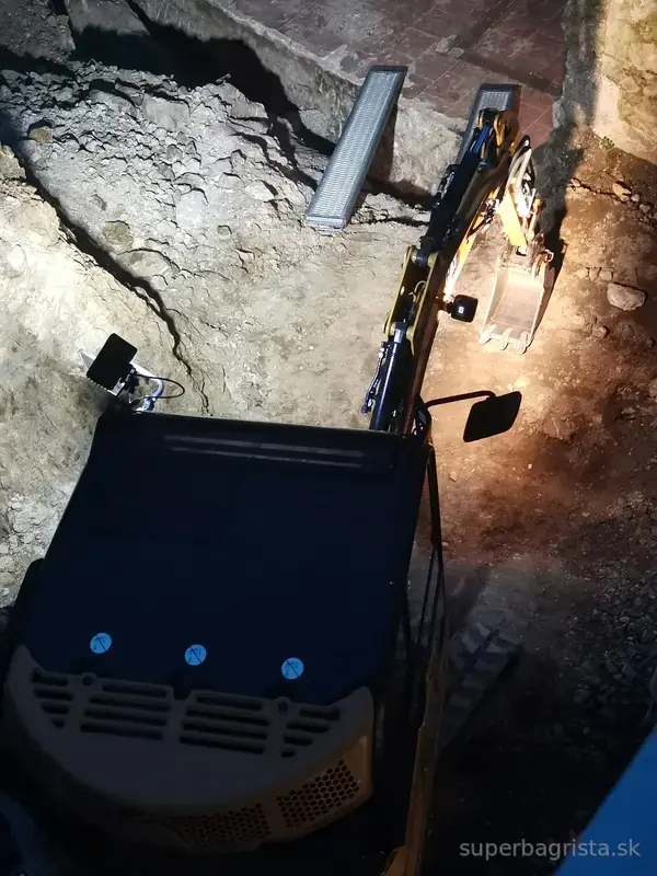 Minibáger CAT pri večernom pokračovaní výkopu v skale