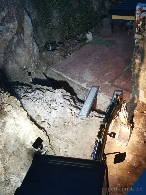 Dokončovanie skalného výkopu minibagrom CAT pri pracovnom osvetlení