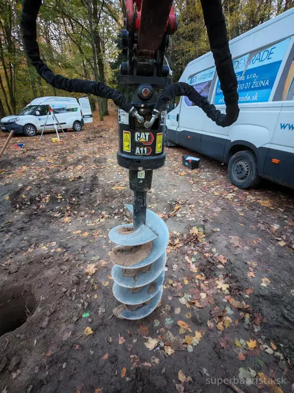 Detail zemného vrtáka zaveseného na ramene minibágra
